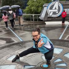Yonah Sienna posing like Spider-man next to the Avengers logo. They are a white androgynous non-binary person with light skin and dark hair